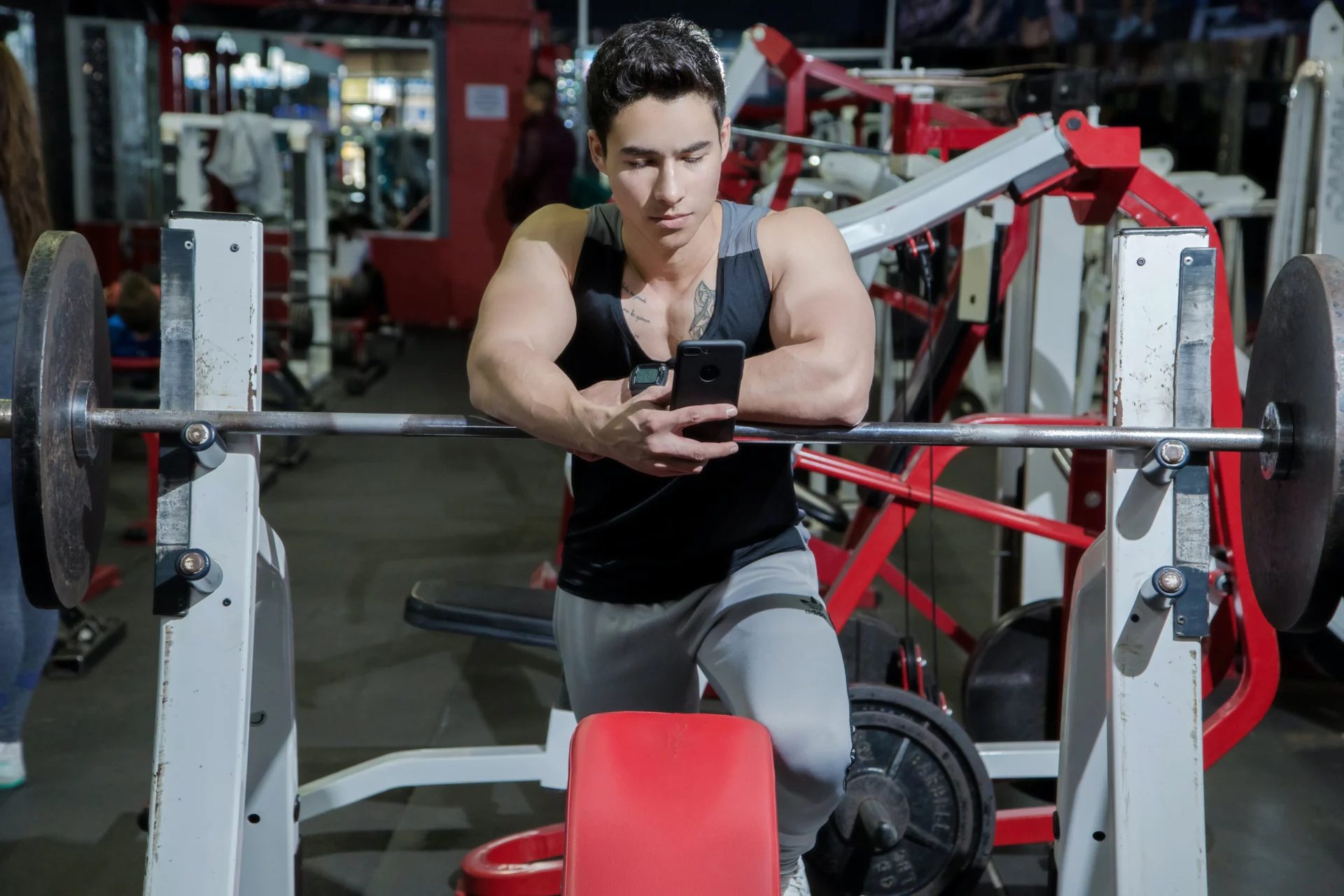 a man with big muscles in a gym on his phone